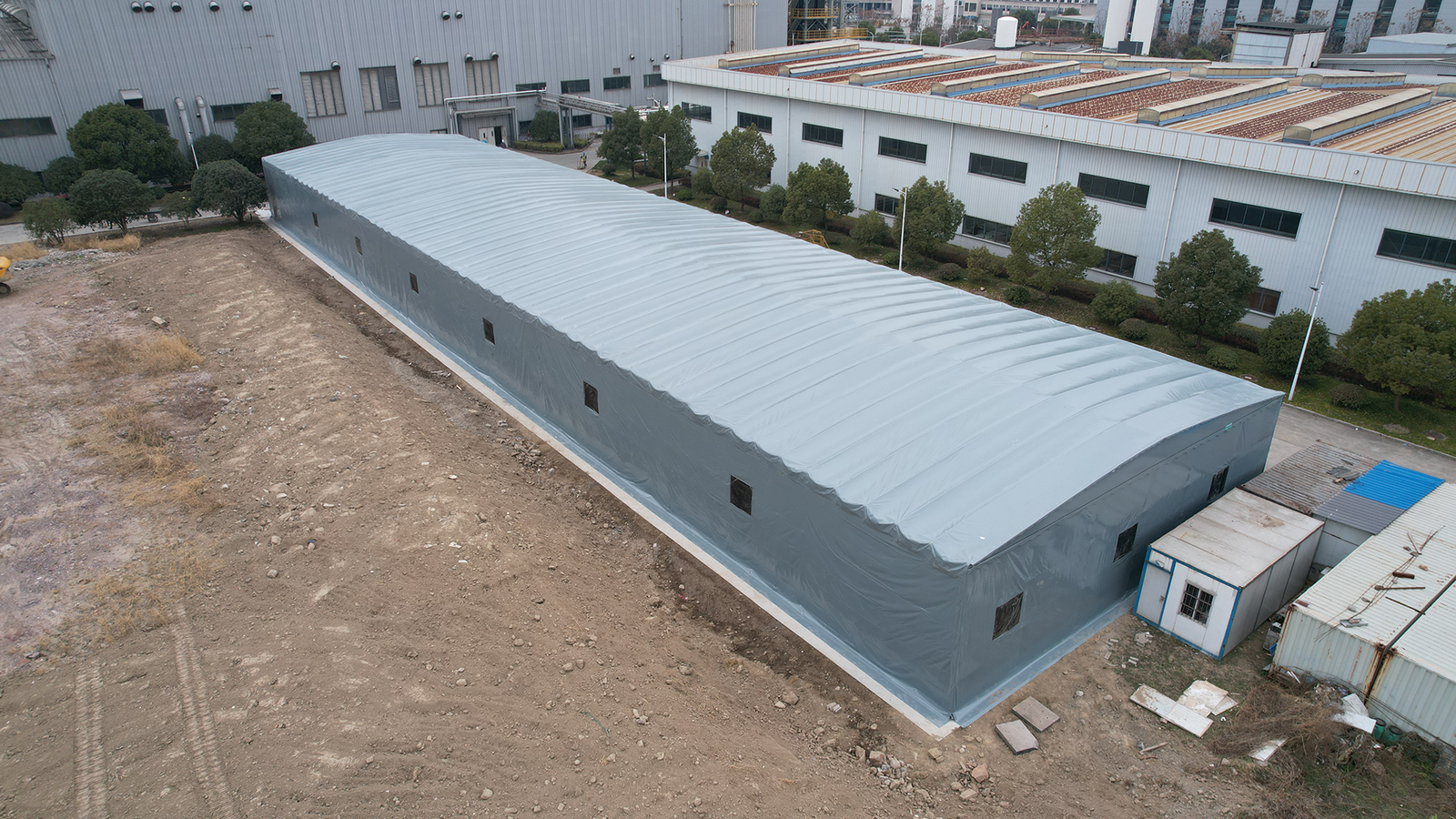 High angle view of a large grey retractable warehouse canopy and temporary fabric storage structure next to a factory building