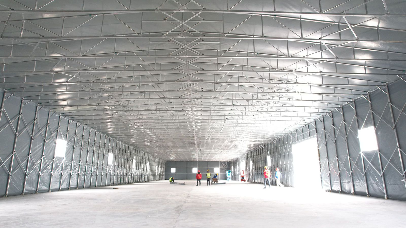 Interior view of a large retractable warehouse canopy showing galvanized light steel frame and scissor truss structure