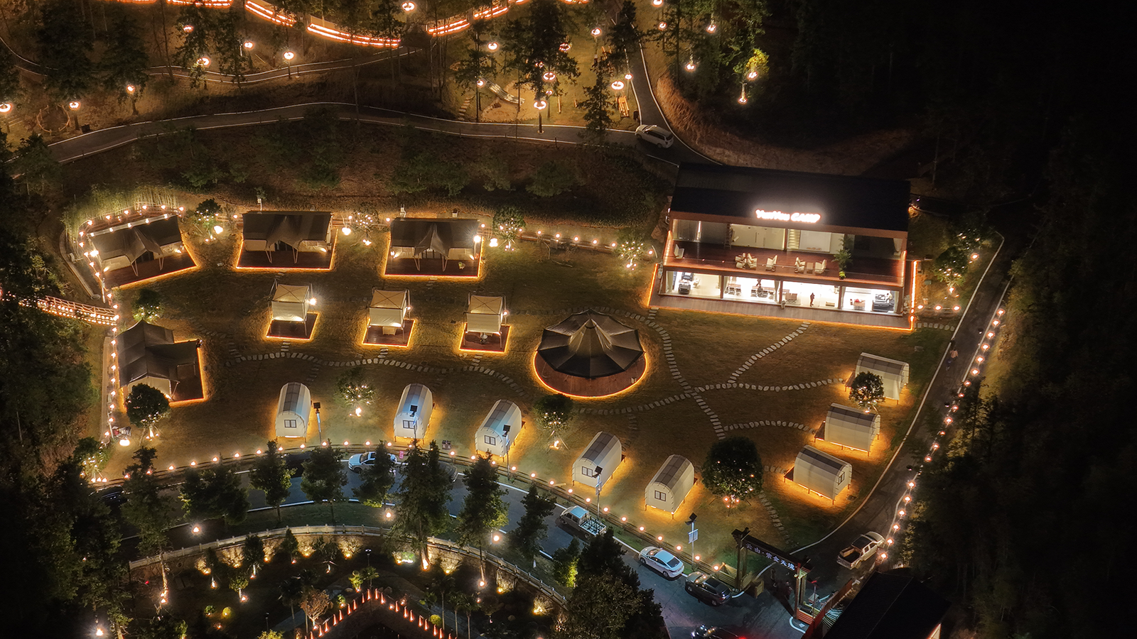 Aerial night view of illuminated luxury glamping resort site plan with glowing tents