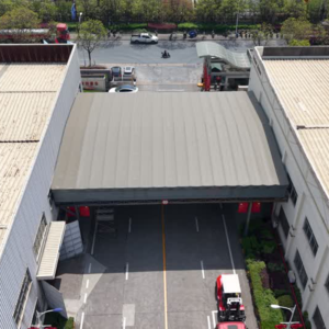 High-angle front view of a large electric retractable canopy extended over a two-lane factory passageway for weather protection