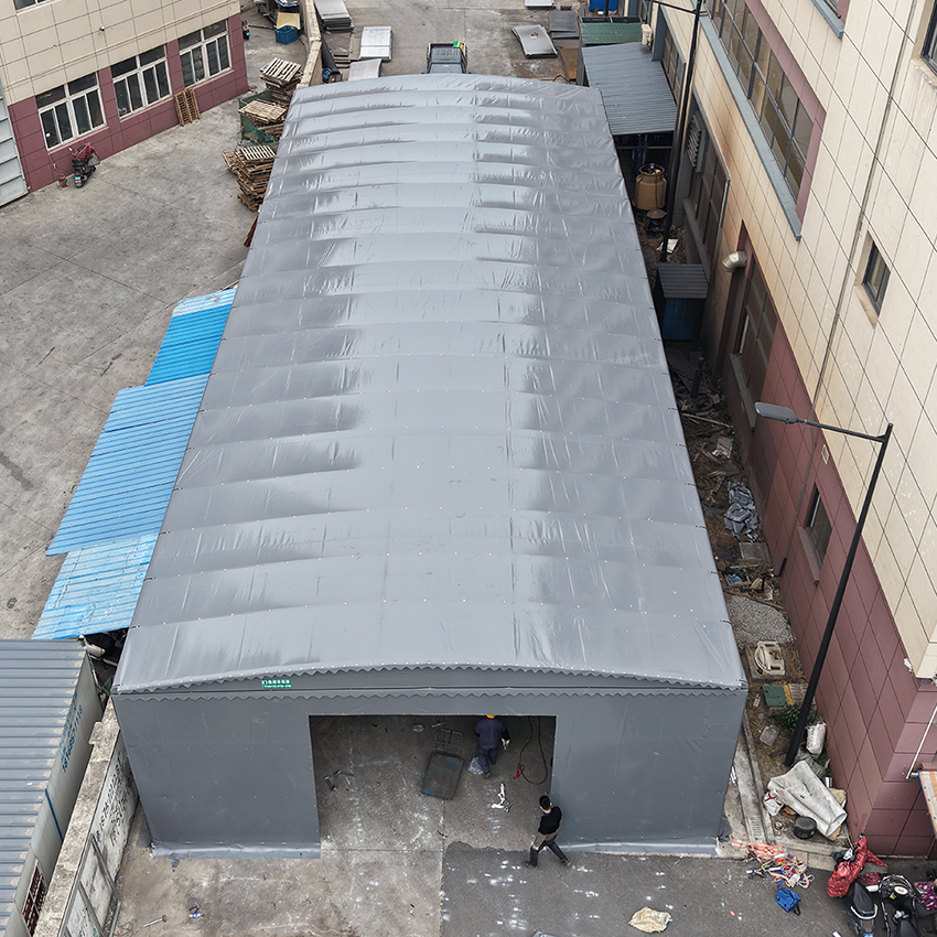 High angle view of a grey heavy duty electric retractable warehouse canopy and temporary industrial storage shelter between factory buildings