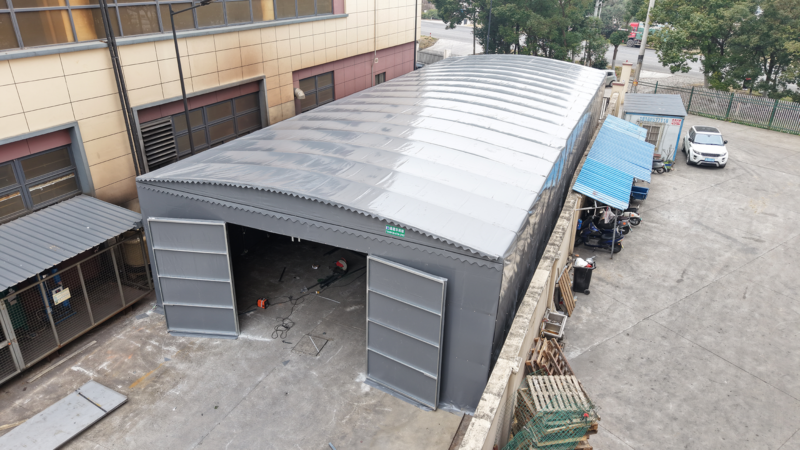 Elevated angle view of a grey motorized retractable warehouse canopy with opened sliding doors in a factory yard
